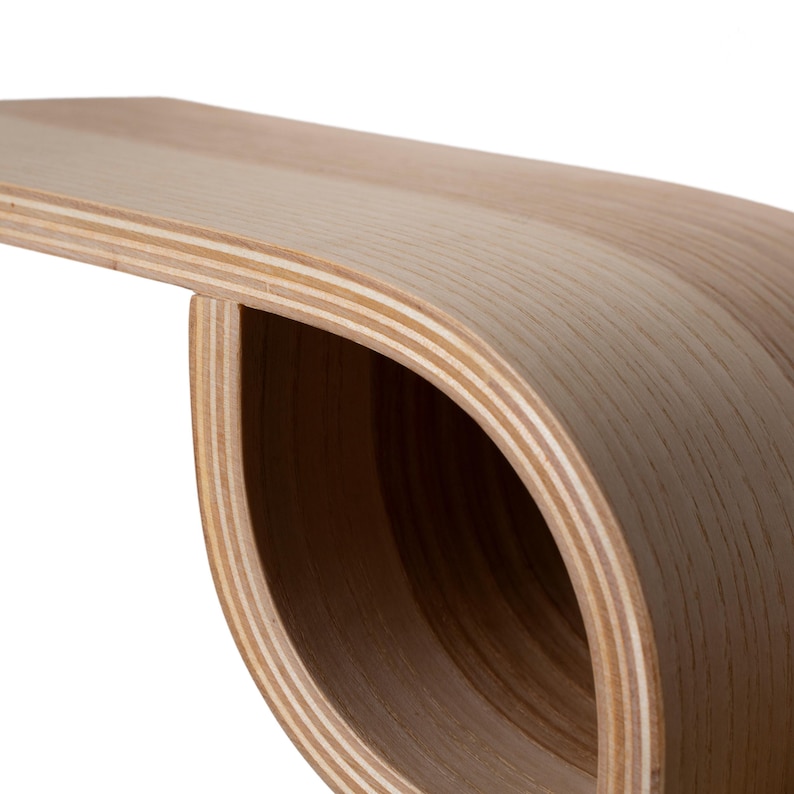 Pu&ograve; includere: Una panca in legno curvata con finitura a venature naturali. La panca ha un design unico e aperto con una forma liscia e arrotondata. Gli strati di legno sono visibili, creando un'estetica moderna e minimalista.