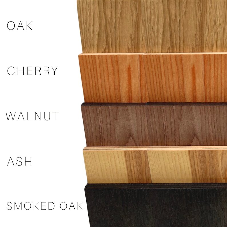 Op de afbeelding: Een close-up van zes houten stalen, elk met een ander nerfpatroon en kleur. De stalen zijn gelabeld met "OAK", "CHERRY", "WALNUT", "ASH" en "SMOKED OAK". De houtkleuren vari&euml;ren van lichtbruin tot donkerbruin en zwart.