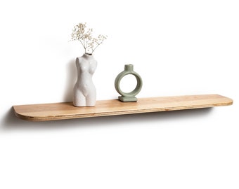 May include: A wooden shelf with rounded edges, featuring a white ceramic vase with dried flowers and a green ceramic ring-shaped vase.