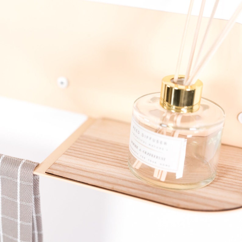 May include: A wooden shelf with a clear glass reed diffuser bottle with a gold lid and wooden reeds. The bottle has a white label that reads "Reed Diffuser - Essential Oil Blend - Lemon & Cardamom - 100 ml".