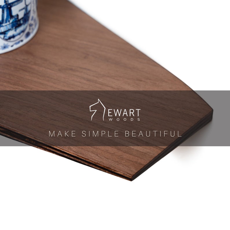 Op de afbeelding: Een close-up van een donkerbruin houten oppervlak met zichtbare houtnerf. Het oppervlak heeft een geometrische vorm met een donkere rand. De tekst "Ewart Woods" en "MAKE SIMPLE BEAUTIFUL" zijn zichtbaar.