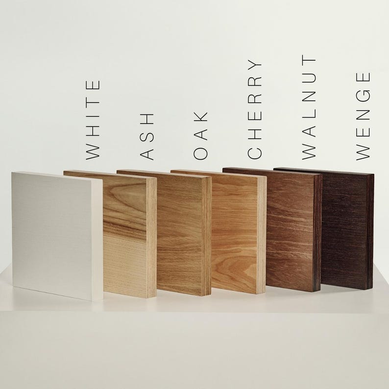 May include: Six rectangular wood samples arranged in a row, labeled White, Ash, Oak, Cherry, Walnut, and Wenge. The samples display varying wood grain patterns and colors, ranging from a solid white finish to light tan, medium brown, and dark brown.