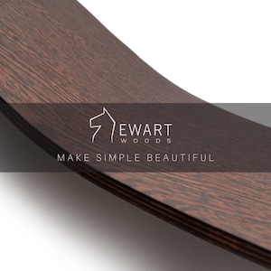 May include: Close-up of a curved, dark brown wooden surface with visible wood grain. The text "EWART WOODS" and "MAKE SIMPLE BEAUTIFUL" are displayed in white. The wood appears to be a rich, dark color.