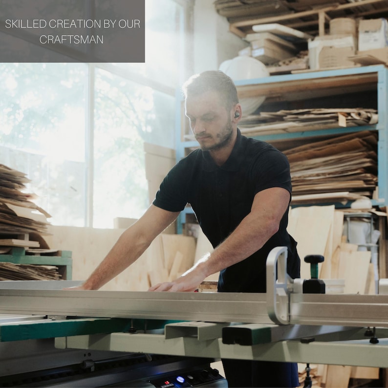 May include: A craftsman working in a wood shop, operating a large saw. The image includes the text "SKILLED CREATION BY OUR CRAFTSMAN". The shop has a window and shelves filled with wood.