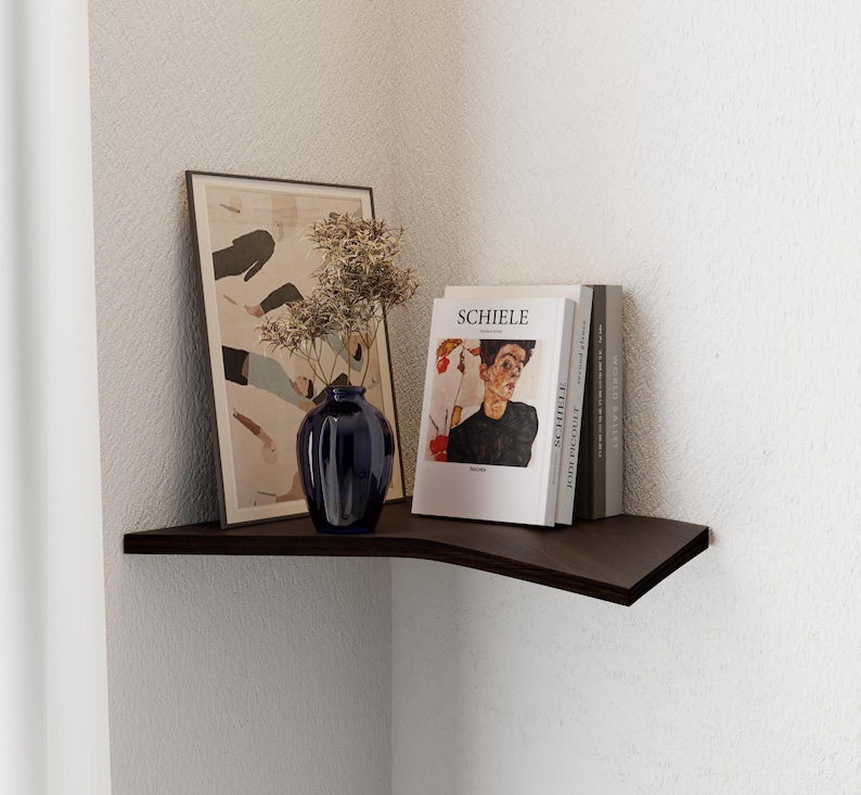 wood corner shelf dark brown with a book, vase painting on top in white corner of the room