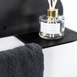 May include: A black shelf with a gray towel hanging from it. A clear glass bottle with a gold lid and a white label that says "Reed Diffuser" is on the shelf.