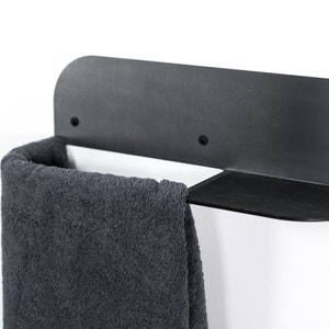May include: Black metal towel rack with a shelf. A gray towel is hanging on the rack.