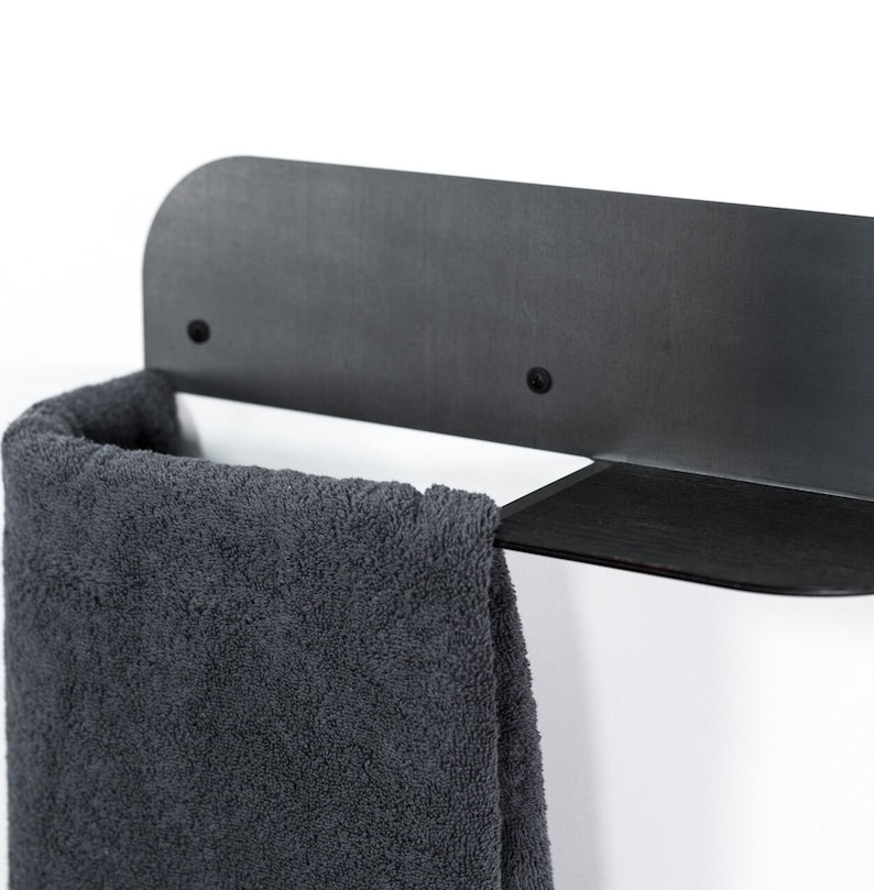 May include: Black metal towel rack with a shelf. A gray towel is hanging on the rack.