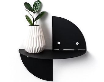 May include: A black, semi-circular wall shelf with a white vase holding a green plant. The shelf is mounted on a white wall. The vase has a geometric design.