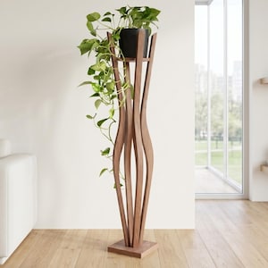 Walnut tall floor plant stand with tropical hanging plant by large bright window. Shows real scale in a living room corner — stand is 118cm/46inch tall. Sculptural 4-leg wooden pillar design suits modern, boho or Scandinavian interiors.