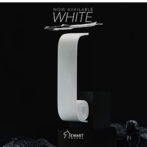 以下が含まれることがあります： ユニークな曲線デザインの白い木製トイレットペーパーホルダー。ホルダーは黒いベースに取り付けられ、上部には「NOW AVAILABLE WHITE」の文字があります。ブランドロゴ「EWART WOODS」が下部にあります。