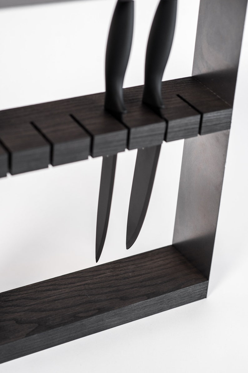 Close-up of a modern knife organizer with a dark wooden block, securing multiple black-handled knives horizontally in precision-cut slots.
