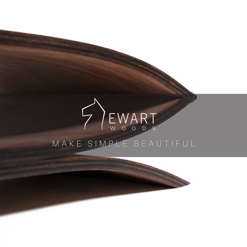 May include: Two curved, dark brown wooden sheets with visible layered grain patterns. The logo EWART WOODS and the text MAKE SIMPLE BEAUTIFUL are printed in white over a gray horizontal bar centered across the overlapping wooden surfaces.