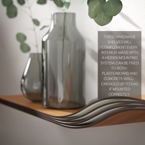 May include: A wooden floating shelf with a wavy design, featuring a dark brown edge and a light brown top. The shelf holds two gray glass vases with plants. Text on the right says the shelf can hold up to 11 pounds.