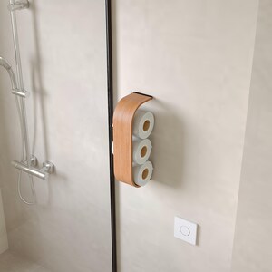 以下が含まれることがあります： 明るい色の壁に取り付けられた木製のトイレットペーパーホルダー。 ホルダーは湾曲したデザインで、3つの白いトイレットペーパーロールを保持します。 ホルダーは、暗いエッジを持つ明るい色の木材で作られています。