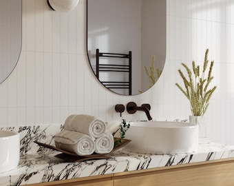 May include: A modern bathroom scene featuring a white vessel sink, a dark bronze faucet, and a marble countertop. Rolled towels rest on a wooden tray. A large oval mirror and a wall-mounted light fixture are also visible.