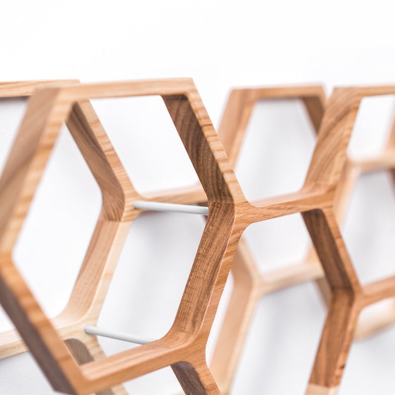 May include: A series of interconnected wooden hexagonal frames featuring a natural light brown wood grain finish. The geometric structures are joined together by thin, cylindrical white metal rods, creating a modular honeycomb-like wall display.