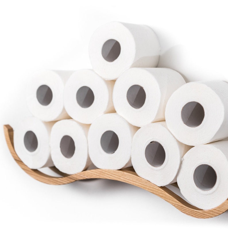 Close-up of a wall-mounted toilet paper holder with a wave design, holding ten rolls of toilet paper. The wave texture is prominently displayed.