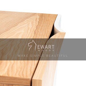 K&ouml;nnte beinhalten: Nahaufnahme eines Holzschranks mit einem wei&szlig;en Kantendetail. Der Schrank ist aus hellem Holz mit nat&uuml;rlicher Maserung. Der Text "Ewart Woods" und "Make Simple Beautiful" ist auf dem Schrank sichtbar.