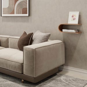 May include: A modern living room scene featuring a beige sectional sofa with brown accent pillows. A wooden floating shelf displays a framed floral print and books. A framed abstract art piece hangs on the wall.