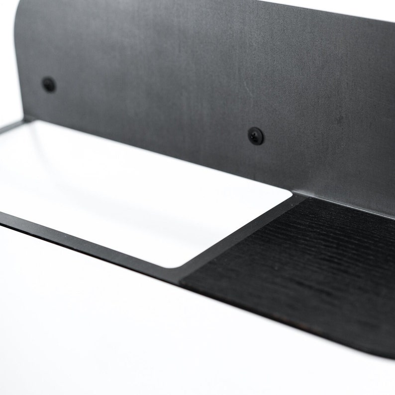 May include: A black metal shelf with a white rectangular shelf and a black wooden shelf. The shelf is mounted to a wall.