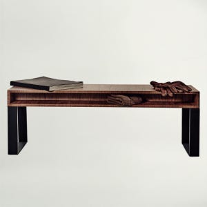 Può includere: Una panca rettangolare in legno con finitura a venature marrone scuro e gambe in metallo nero. La panca presenta un ripiano orizzontale contenente un libro nero, un tessuto a maglia marrone piegato e un paio di guanti in pelle marrone.