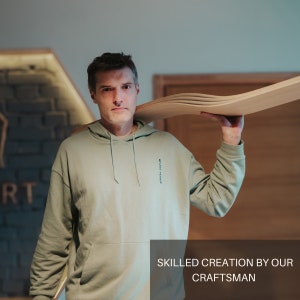 May include: A man in a light green hoodie carries a stack of wood planks on his shoulder. The text "SKILLED CREATION BY OUR CRAFTSMAN" is at the bottom of the image.