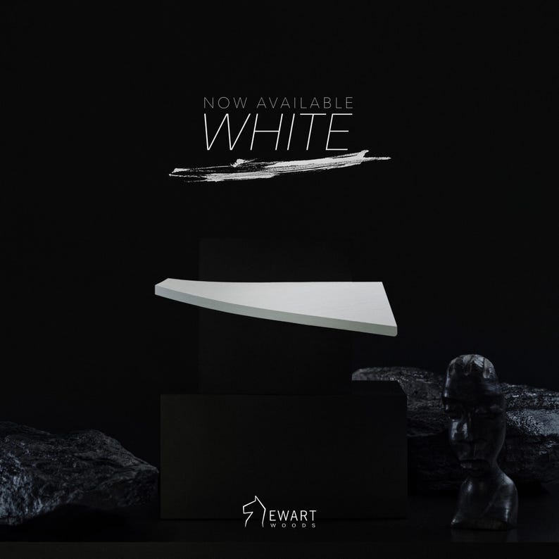Op de afbeelding: Een witte, driehoekige plank wordt weergegeven tegen een zwarte achtergrond. De tekst "NOW AVAILABLE WHITE" staat boven de plank. Het Ewart Woods-logo staat onderaan. De plank lijkt van hout te zijn.