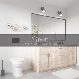 May include: A bathroom interior featuring a light wood vanity with black hardware, a large rectangular mirror, and two wall-mounted lights. A white toilet sits near a wall-mounted hexagonal wooden toilet paper holder. The text Ewart Woods Make Simple Beautiful is visible.