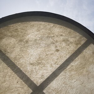 May include: A close-up of a brown leather drum with a dark brown rim. The drum is partially visible against a blue sky with white clouds.
