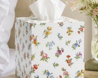 May include: A square tissue box cover featuring a white background with a scattered pattern of small, colorful botanical illustrations including pink roses, yellow pansies, blue cornflowers, and green leaves, with a white tissue protruding from the top.