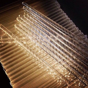May include: A stack of clear glass rods, arranged in a criss-cross pattern, with a golden glow reflecting off the surface.