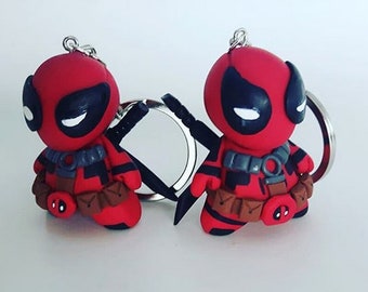 May include: Two red and black Deadpool keychains. Each keychain features a small, stylized figure of the Marvel Comics character, with black accents and a silver keyring. The figures are posed with their arms out, holding black swords.