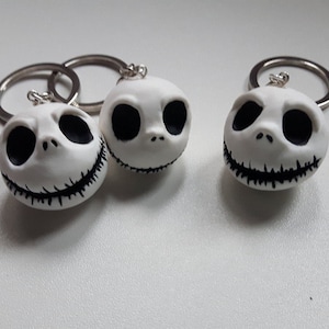 Puede incluir: Tres llaveros blancos de Jack Skellington con rasgos faciales negros y un llavero plateado. Los llaveros son redondos y tienen una boca sonriente. Los llaveros son un artículo de novedad.