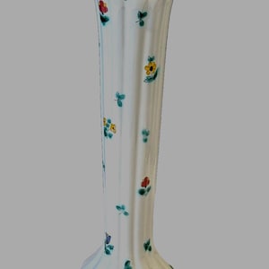 Op de afbeelding: Een witte keramische vaas met een gegolfde rand en een groene rand. De vaas is versierd met een bloemenpatroon in tinten geel, rood, groen en blauw.