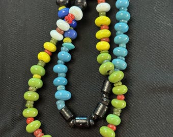 May include: A colourful beaded necklace with red, green, blue, yellow, and white beads. The necklace is made of glass beads and has a black wooden clasp.