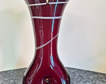 May include: A burgundy glass vase with white stripes. The vase has a wide mouth and a round base.