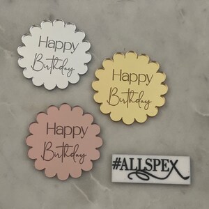 May include: Three round, scalloped acrylic cake toppers with the text "Happy Birthday" in a cursive font. The toppers are in silver, gold, and rose gold.
