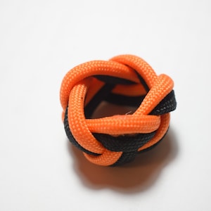 May include: A black and orange paracord knot, also known as a monkey fist knot, is a decorative knot that can be used as a keychain or a small weight.