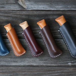 Può includere: Sei foderi per coltelli in pelle di diversi colori, tra cui blu, marrone e bordeaux. Ogni fodero presenta un dettaglio di cucitura bianca e un manico in legno che sporge.