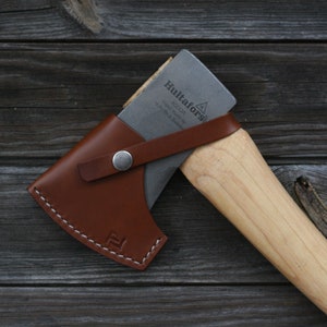 May include: A brown leather axe sheath with a metal snap closure and a Hultafors axe with a wooden handle.