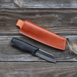 May include: A black handled knife with a brown leather sheath. The knife has a black handle and a silver blade. The sheath is made of brown leather and has a white stitching detail.