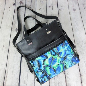 May include: A black leather tote bag with a blue and green butterfly print lining. The bag has a top zipper closure, two front pockets, and a shoulder strap.