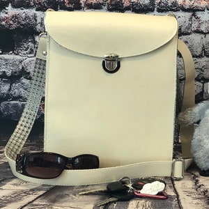 May include: A cream-colored leather crossbody bag with a silver clasp. The bag has a patterned strap and is shown with sunglasses and keys.