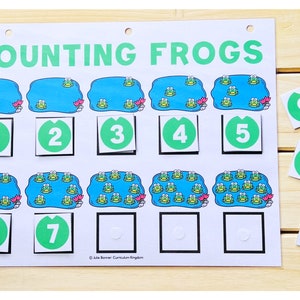 May include: A counting game for kids featuring frogs in lily pads. The game includes ten green squares with numbers 1 through 10. The numbers are placed in the squares below the lily pads with frogs.