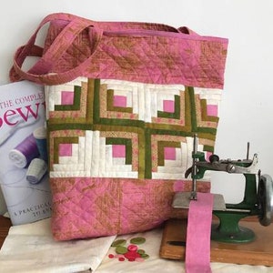 May include: A pink quilted tote bag with a patchwork design featuring squares of pink, white, and green fabric. The bag has a long strap and is made with a quilting technique called "log cabin".