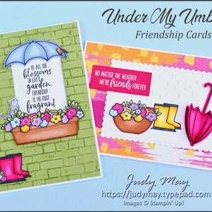 May include: Two handmade greeting cards with a friendship theme. The first card features a green brick background with a window box of flowers and a blue umbrella. The second card has a colourful abstract background with a window box of flowers, a yellow pair of rain boots, and a pink umbrella. Both cards have text that reads "Of all the blossoms in life's garden, friendship is the most fragrant." and "No matter the weather we're friends forever."