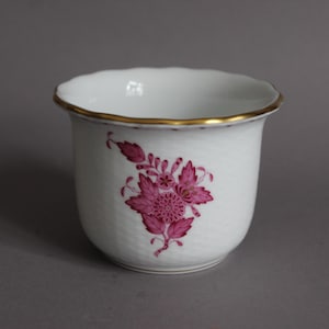 May include: White ceramic planter with a scalloped rim and a gold band. The planter features a floral design in shades of pink. The interior is white, and the exterior has a textured surface.