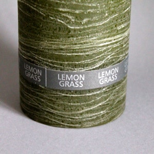 May include: A green pillar candle with a textured surface and a label that reads "LEMON GRASS".