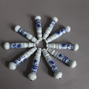May include: A set of nine cylindrical ceramic handles arranged in a circular pattern. Each handle features a white base with a blue floral pattern, a smooth glossy finish, and rounded ends, creating a uniform look for cabinet or drawer hardware.